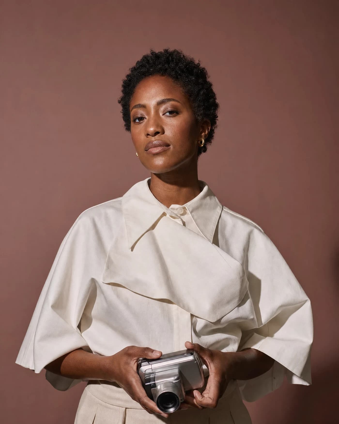 Editorial portrait of a creator holding a video camera against a rose backdrop